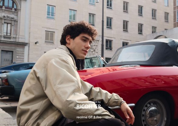 Portrait en extérieur d'un jeune homme posant à côté d'une voiture de sport rouge décapotable, mentionnant le realme GT 8 Pro (Ricoh GR).