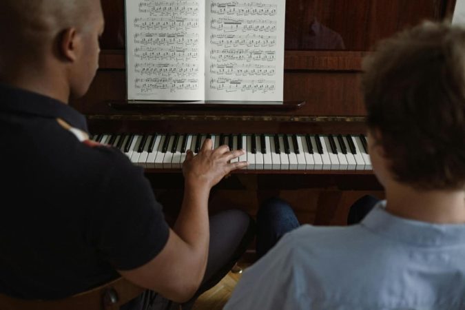 Un enseignant montre une technique de jeu à son élève sur un clavier lors d'un cours de piano de dos.