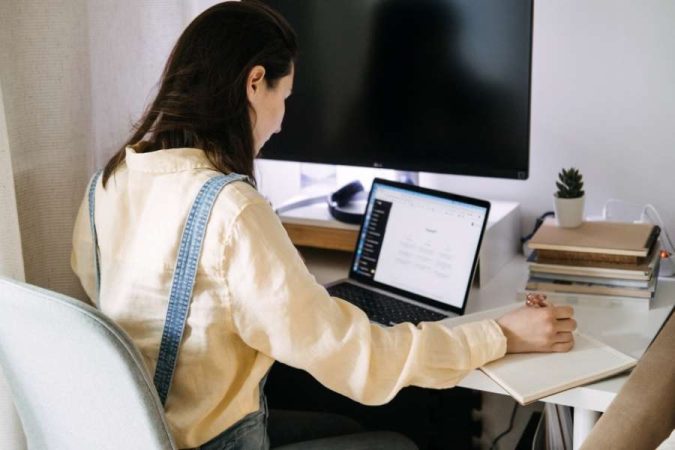 Une femme assise à son bureau analyse des données sur son ordinateur portable pour choisir entre ChatGPT et Gemini.
