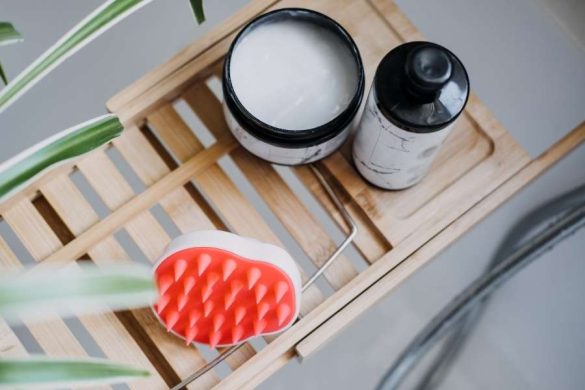 Un pot de crème et une brosse massante en silicone sur un support en bois pour le gommage du cuir chevelu.