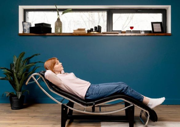 Femme rousse allongée les yeux fermés sur un fauteuil de massage domicile dans un salon moderne.