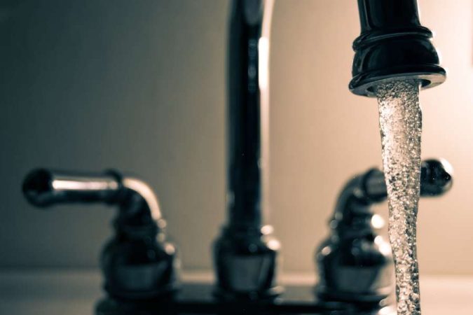 Gros plan sur un robinet de lavabo en chrome brillant qui laisse couler un flux d'eau régulier, provoquant parfois un bruit strident.