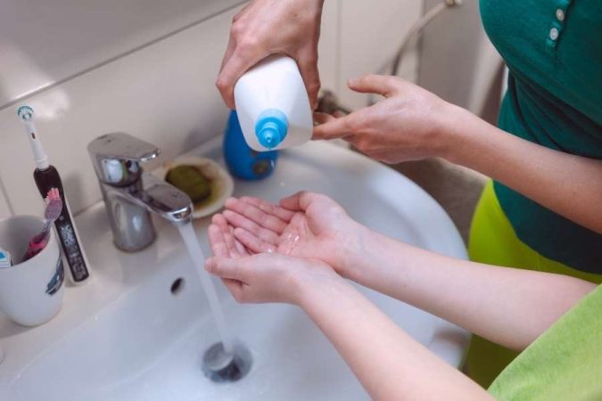 Un adulte verse du savon dans les mains d'un jeune enfant au-dessus d'un lavabo pour enseigner les règles de propreté à son enfant.