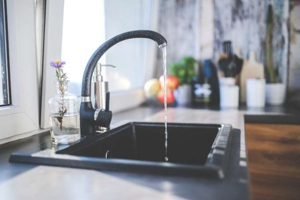 Robinet de cuisine noir moucheté en fonctionnement au-dessus d'un évier encastré dans un plan de travail moderne.